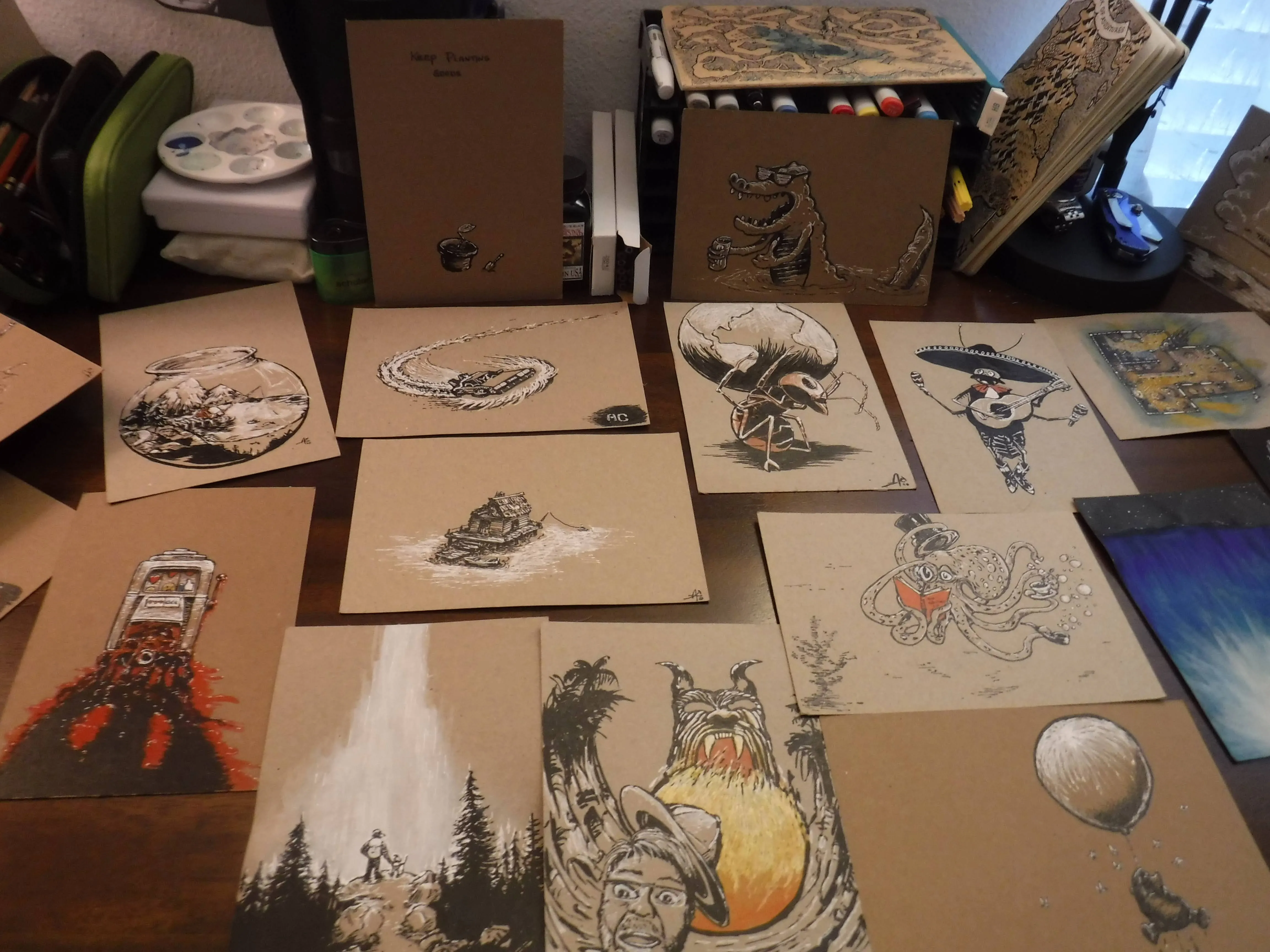 A studio table covered with whimsical ink and watercolor drawings on warm brown paper