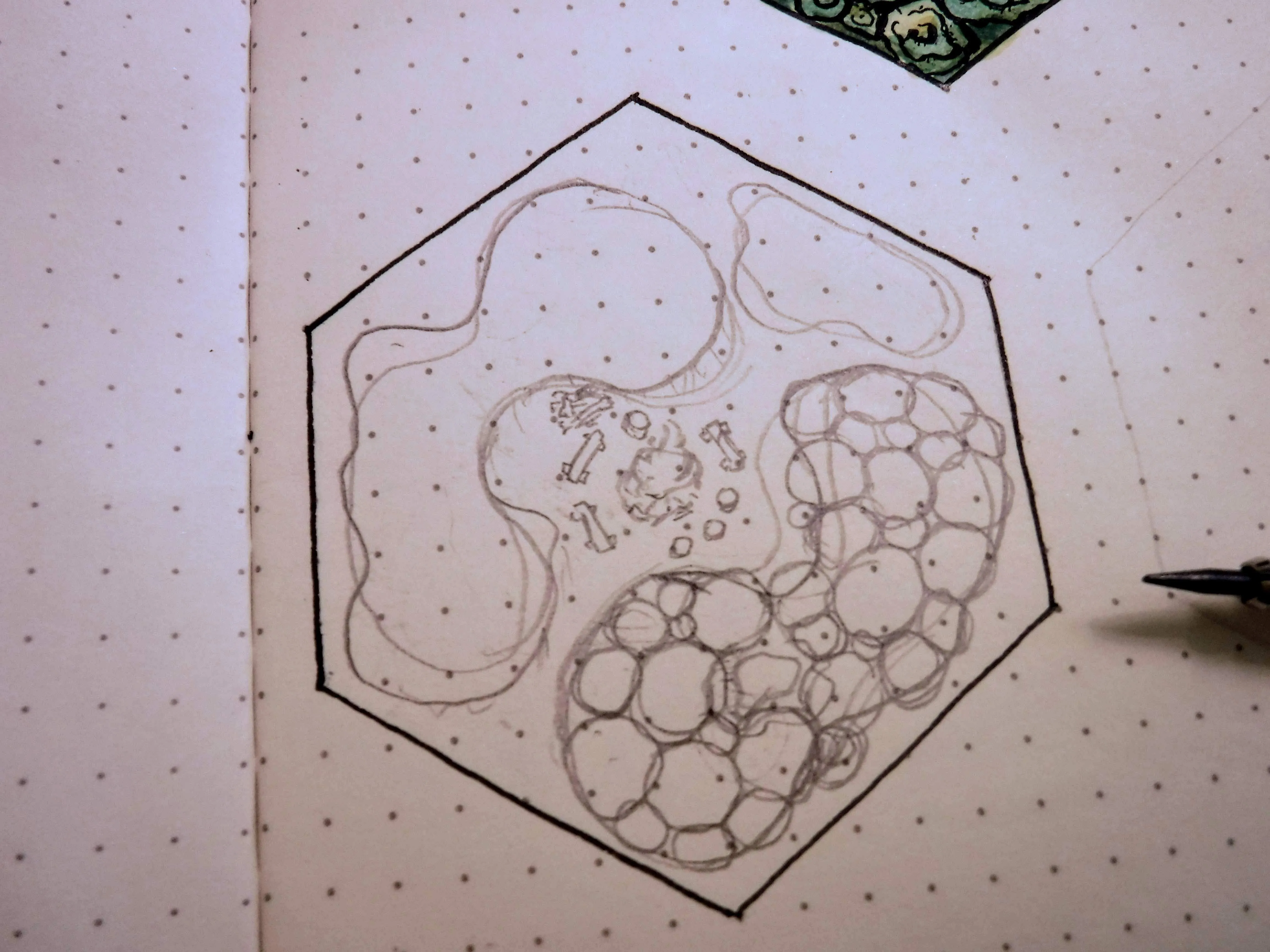 A penciled fantasy map hex in progress on a dotted sketchbook page beside a drawing pen